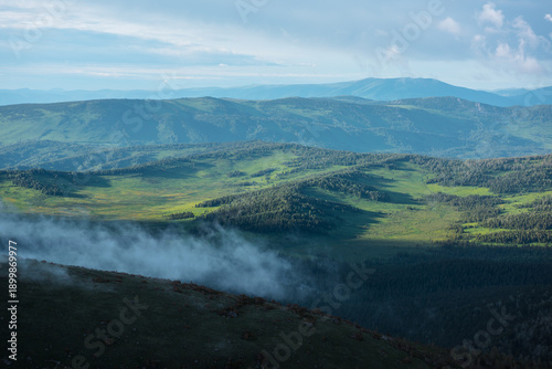 Photos Scenic aerial top view from above through low cloud on pass to green hilly vastness and layered mountain silhouettes far away under dramatic cloudy sky