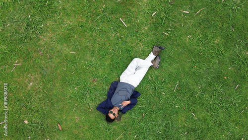 Εκτύπωση καμβά A man is laying on the grass, holding a cell phone