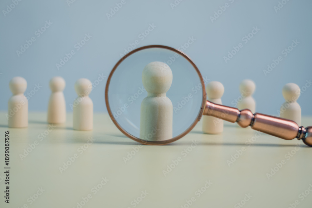 Obraz premium Wooden human figures with a magnifying glass symbolize recruitment, talent search, human resources, candidate selection, hiring process, leadership, and business decision concept.
