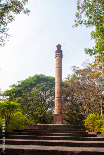 Fényképezés Ancient Ashokan pillar at Dhauli, Odisha rises on stepped platform, crowned with lion capital, surrounded by greenery, symbolizing Mauryan heritage, peace, and Buddhism