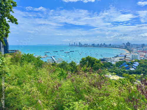 Panoramic view of Pattaya blue bay with hundreds of boats seen from the high hilltop. The photo covers the beautiful arc-shaped coastline, with the sea surface dotted with white tourist boats