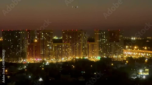 Wallpaper Mural Vibrant orange and blue sunset over a modern city skyline with illuminated residential apartment buildings and a lone airplane in the sky, capturing an atmospheric urban evening. Torontodigital.ca