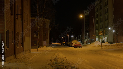 Snowy residential street at night with yellow street lighting.