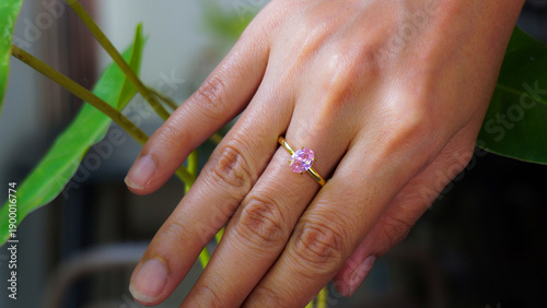 Woman hand wearing gold ring with pink gemstone on finger with green leaves, elegant jewelry lifestyle and romantic fashion concept