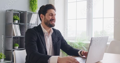 Online meeting with partners or colleagues of happy businessman, telework in office workplace. Man sitting at table with laptop, smiling and talking in remote interview, success of video call