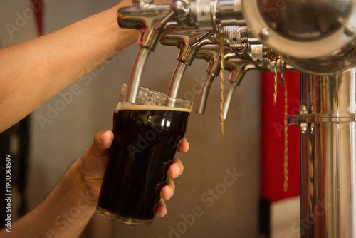 Vászonkép Fresh dark craft beer being poured from stainless steel tap into a glass at a brewery bar