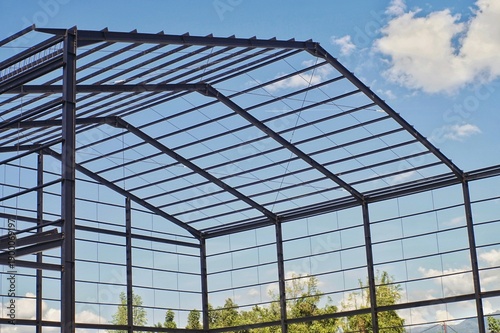 Steel frame structure of a new industrial building or warehouse under construction against a blue sky with clouds.