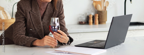 Bild auf Leinwand Woman at the table with a glass of wine in her hands, laptop on the table