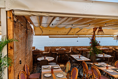 Outdoor restaurant dining terrace in Menorca with tables and chairs overlooking the peaceful Mediterranean Sea