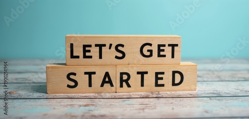Wallpaper Mural Wooden blocks spell LETS GET STARTED on a textured surface against a teal background. This visual signifies beginning new ventures, projects, or phases with positive intent and readiness for action. Torontodigital.ca