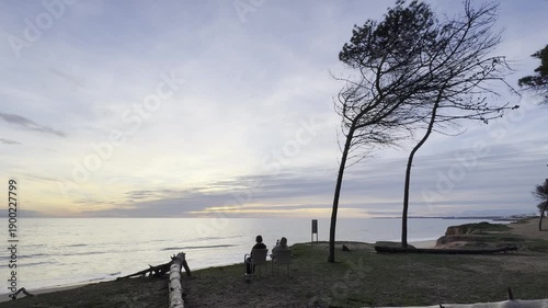 mother and daughter sitting on sandy beach on sunset on spring day. Back view. beach on Algarve coast in Portugal