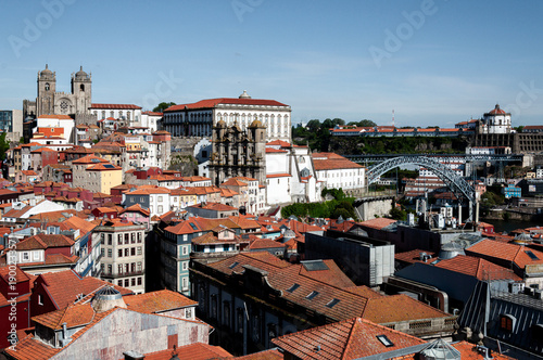 Looking over the rooftops of the old town of Porto towards the city cathedral and the iconic Dom Louis 1 bridge under a blue sky