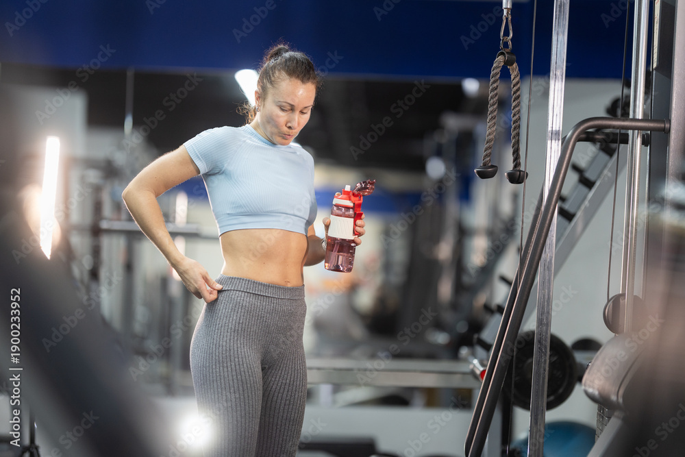 Fototapeta premium Woman checking fitness progress holding water bottle at gym
