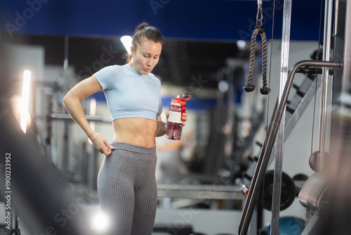 Woman checking fitness progress holding water bottle at gym