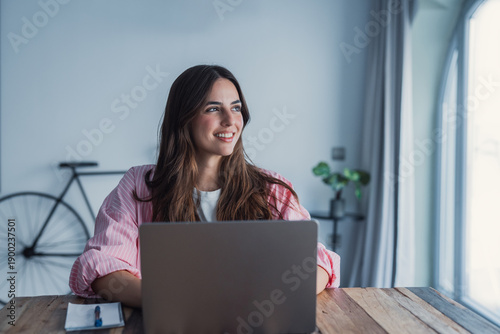 Konstfotografi Dreamy young woman pondering ideas, sitting at desk with laptop, distracted from