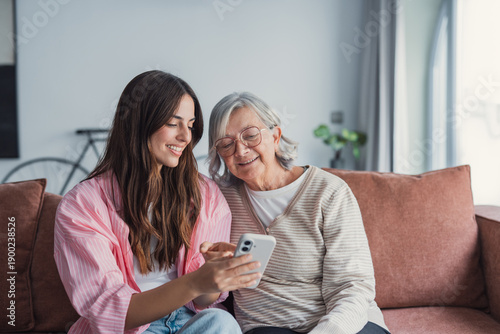Billede på lærred A happy mature mother and her grown daughter sit on a cozy couch at home, huggin