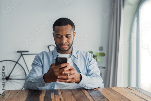 Cuadro en lienzo Confused African guy holding smart phone feels concerned thinking over received message