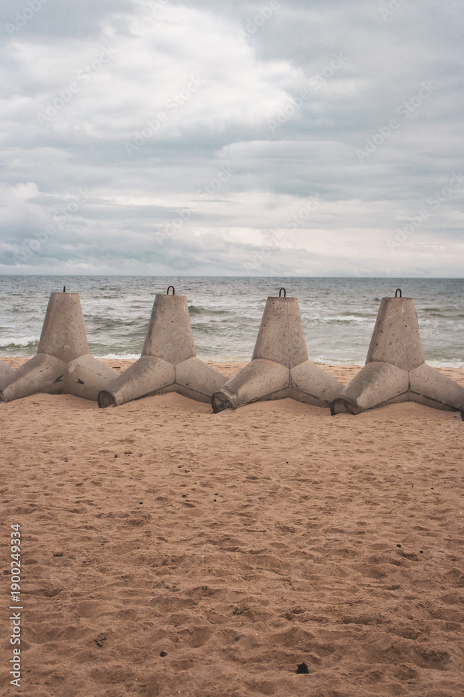 Fototapeta premium Tetrapods on the beach, Ukraine. Winter seascape with barrier blocks against russian invasion.Ukrainian coastal defense. Tetrapod in a row on sand. Seaside during war. Black Sea landscape 