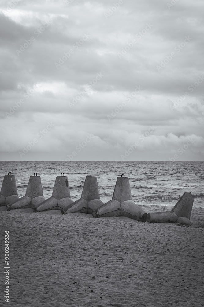 Fototapeta premium Tetrapods on the beach, Ukraine, black and white. Winter seascape with barrier blocks against russian invasion.Ukrainian coastal defense. Tetrapod in a row on sand. Seaside during war. 