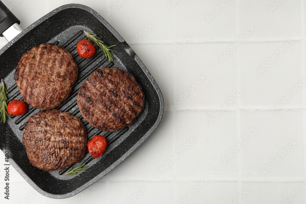 Fototapeta premium Delicious grilled meat patties, tomatoes and rosemary in grill pan on white tiled table, top view. Space for text
