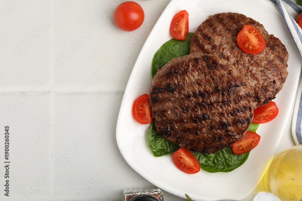 Naklejka premium Delicious grilled meat patties, tomatoes and spinach on white tiled table, flat lay. Space for text