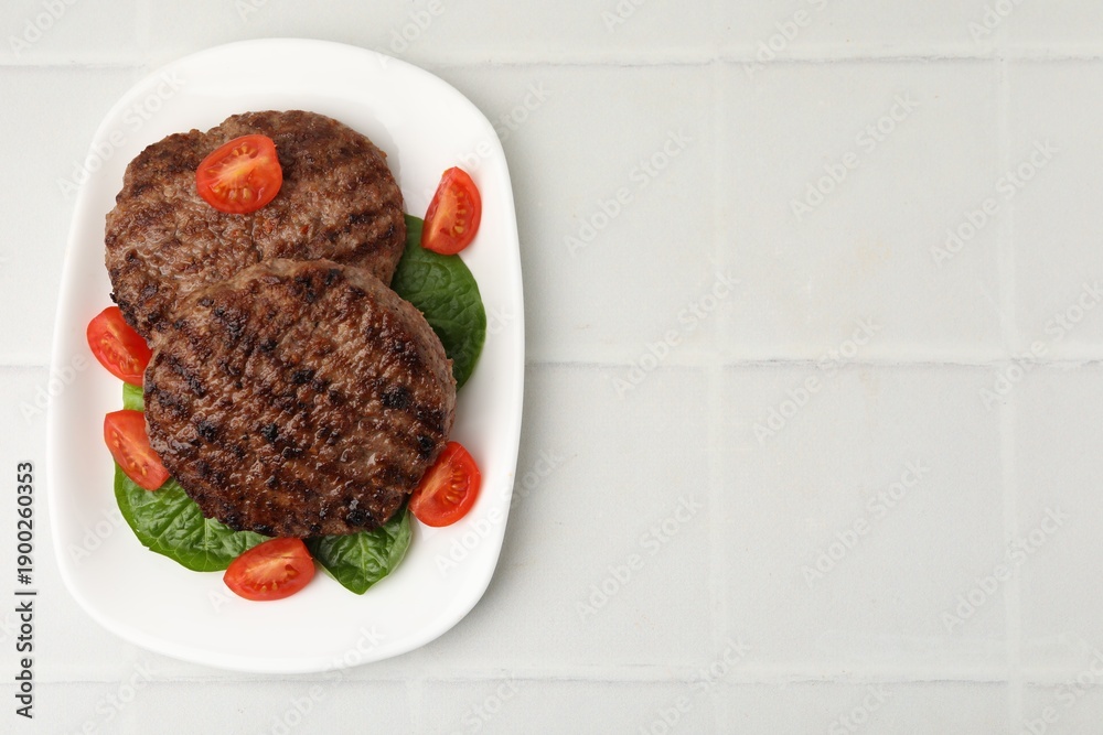 Naklejka premium Delicious grilled meat patties, tomatoes and spinach on white tiled table, top view. Space for text