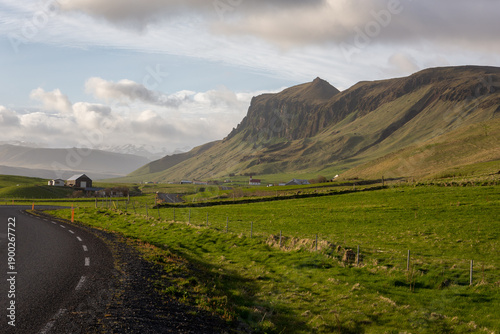 Asphalt curve of the Ring Road passing green grasslands and Eyjafjoll mountains, Iceland