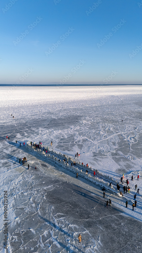 Fototapeta premium Frozen Baltic Sea At Beach With Ice Covered Old Wooden Pier And People Walking On The Ice Enjoying A Sunny Winter Day Scenic Latvia 4K Footage For Travel Nature Seasonal Projects