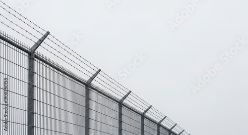 Barbed wire on top of a metal fence against a clear sky. Security and boundary concept for restricted areas.