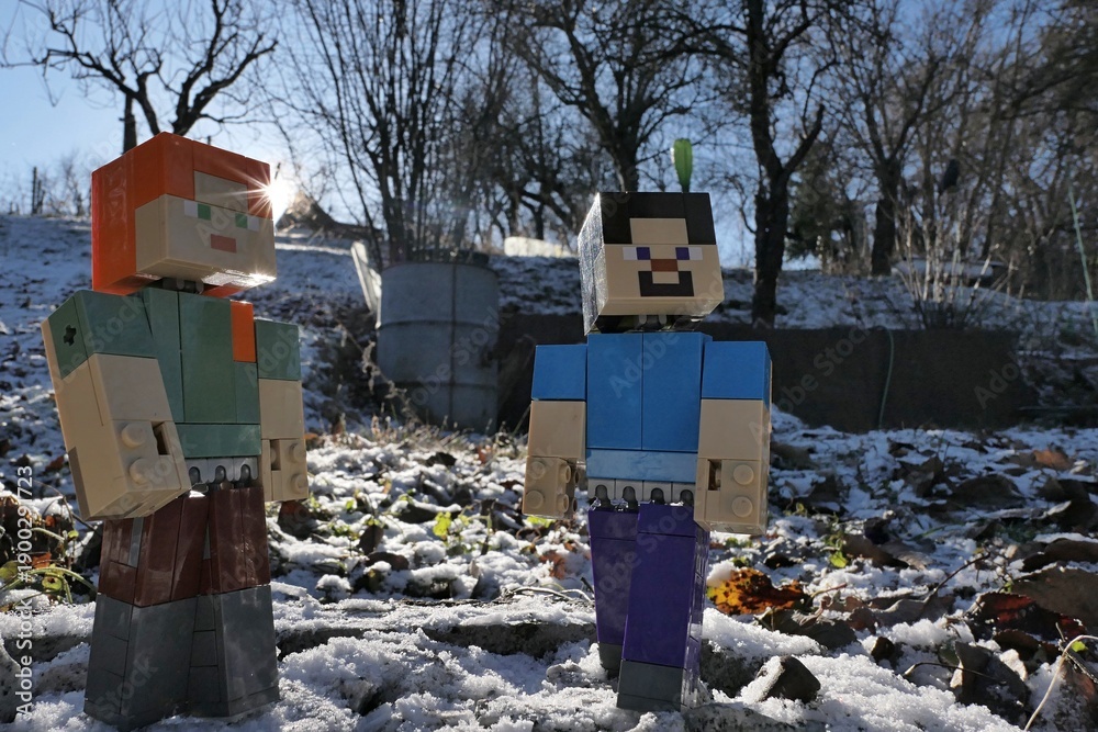 Obraz premium Minecraft figures of Steve and Alex standing in winter garden with sun behind their backs, first snow on the ground. Older steel water barrrel and fruit trees visible in background. Clear blue skies. 