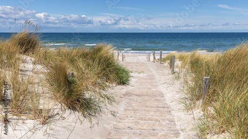 Holzweg durch Dünen mit Strandhafer zum Strand der Ostsee mit blauem Himmel mit Wolken. Ostseebad Rerik in Mecklenburg-Vopmmern, Deutschland