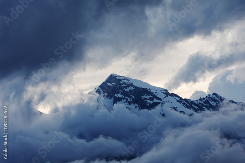 Der schneebeckte Gipfel des Großen Wiesbachhorns in Salzburg, Österreich in den Alpen (Hohe Tauern),  eingehüllt in dunkle Wolken am Abend mit der Sonne hinter dem Berg.