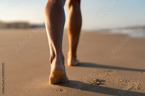 Foto Close-up of toned female legs walking barefoot along the sandy beach in soft morning light, leaving footprints behind on the warm, wet sand with gentle ocean blur in background