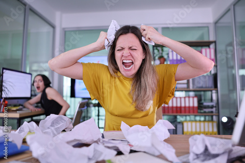 Vászonkép In a bustling office, a woman with long hair yells in frustration while holding her head