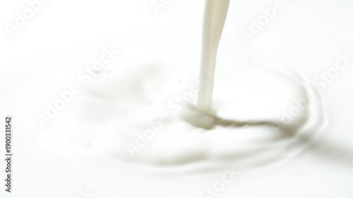 A dynamic, high-key abstract close-up shot captures a thick stream of pure white milk pouring down, creating fresh ripples on the liquid surface in a clean studio setting.