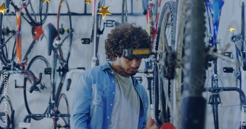 Repairing man wearing denim shirt, checking rear wheel at bicycle shop with wall-mounted bikes