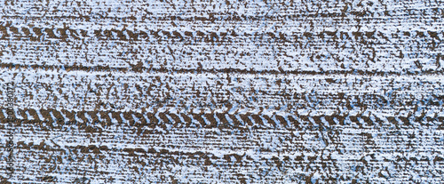 Aerial texture of tire tracks and machinery marks in a snowy field creating a linear industrial pattern in winter