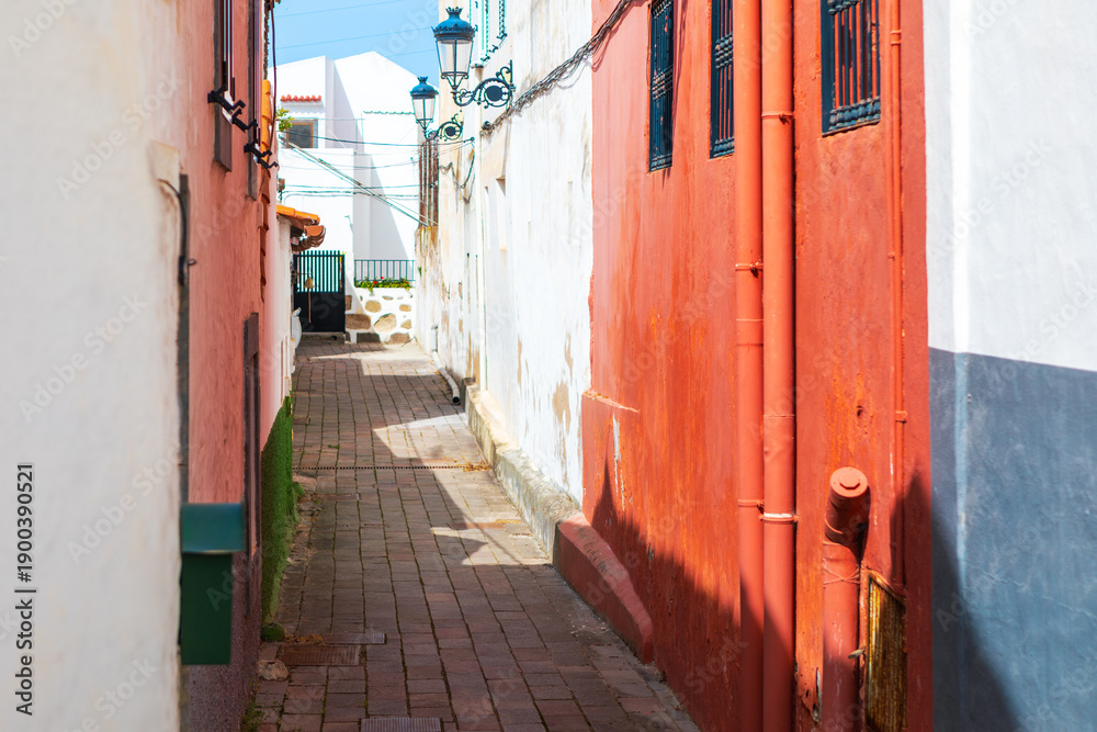 Naklejka premium Narrow alleyway features vibrant stucco walls with traditional ironwork and brick paving. Picturesque scene captures typical old-world Mediterranean architecture found in historic European towns