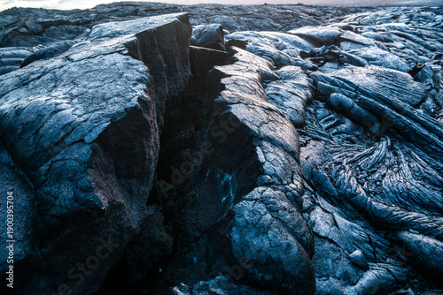 Hardened lava flow forming dramatic rock textures across a volcanic landscape on the Big Island, Hawaii, United States, under overcast sky.