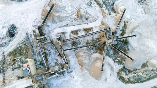 High angle overhead view of industrial machinery and multiple conveyor lines at a snowy mining site in a cold winter environment