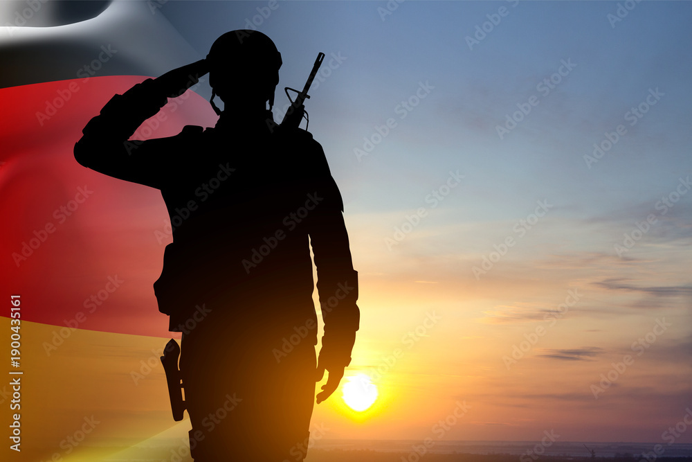 Obraz premium Silhouette of saluting soldier with Germany flag against the sunset. National Holidays concept