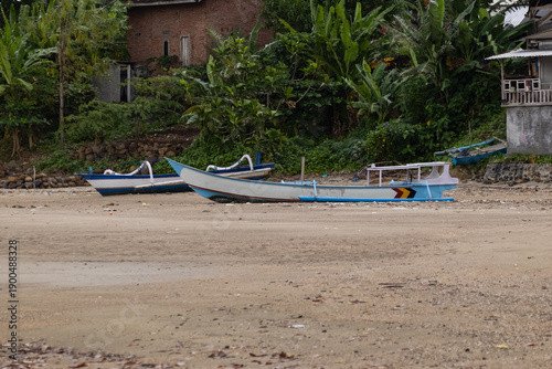 Photos Traditional fishing boats resting on sand beach shoreline with tropical jungle background and village houses