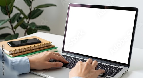 Person Typing On Laptop With Stack Of Books And Smartphone On Desk With Green Plant In Background