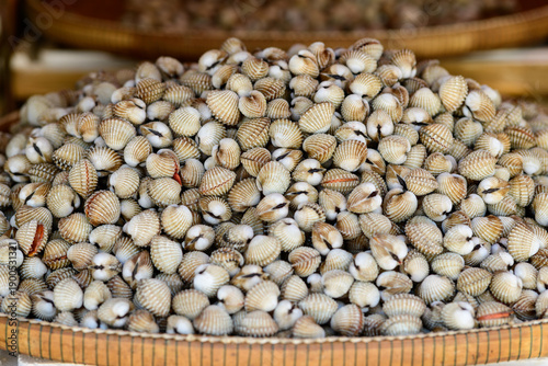 Quadro su tela A detailed view of a large pile of cockle shells displayed in a woven bamboo tray at an outdoor market in Battambang, Cambodia