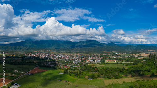 Принти на полотні A wide aerial panorama captures Vang Vieng, Laos, nestled in a lush valley with scattered buildings and vibrant fields