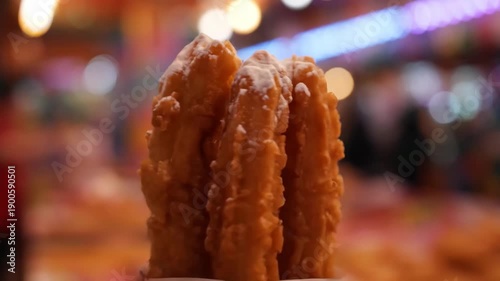 Golden Churros Dusted with Powdered Sugar Held Up Close Against a Blurry Night Fair Background with Festive Bokeh Lights