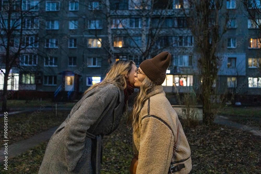 Φωτογραφία Two women greeting with cheek kiss in winter evening residential city