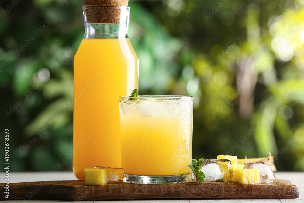 Fototapeta premium Glass and bottle of fresh pineapple juice with mint leaves on white tile table outdoors