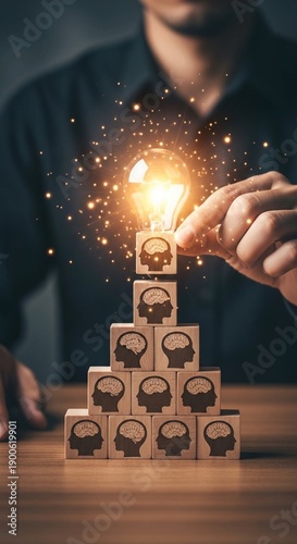 Hand Placing Glowing Light Bulb on Pyramid of Wooden Blocks with Human Brain Icons – Concept of Collective Intelligence, Creative Teamwork, and Leadership