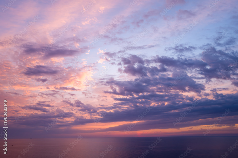 Fototapeta premium Soft lavender and peach clouds drift across a tranquil Mediterranean Sea at sunset, with gentle light reflecting on the water and creating a peaceful, atmospheric mood.